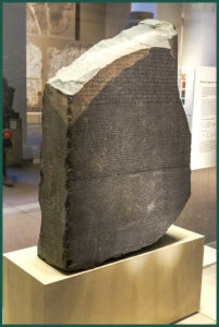 “Stele di Rosetta” frammento di una stele in granodiorite grigia e rosa, recante un decreto sacerdotale riguardante Tolomeo V suddiviso in tre blocchi di testo: geroglifico (14 righe), demotico (32 righe) e greco (54 righe), attualmente custodito presso il British Museum a Londra.